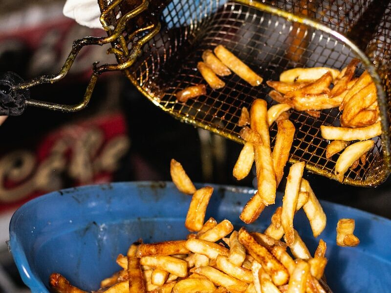 person transferring fries from basket to a bowl